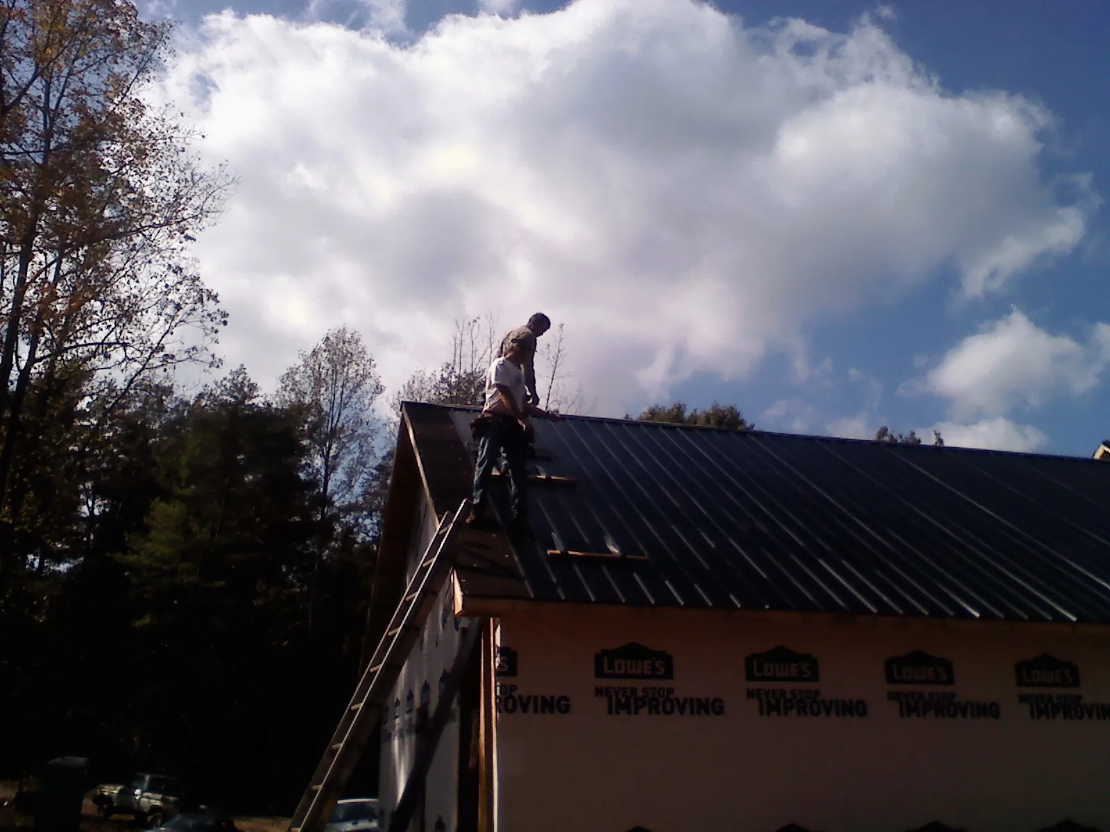 Roofer fastening dark metal panels high against a cloudy sky, from a Roof Inspection job in Port Royal