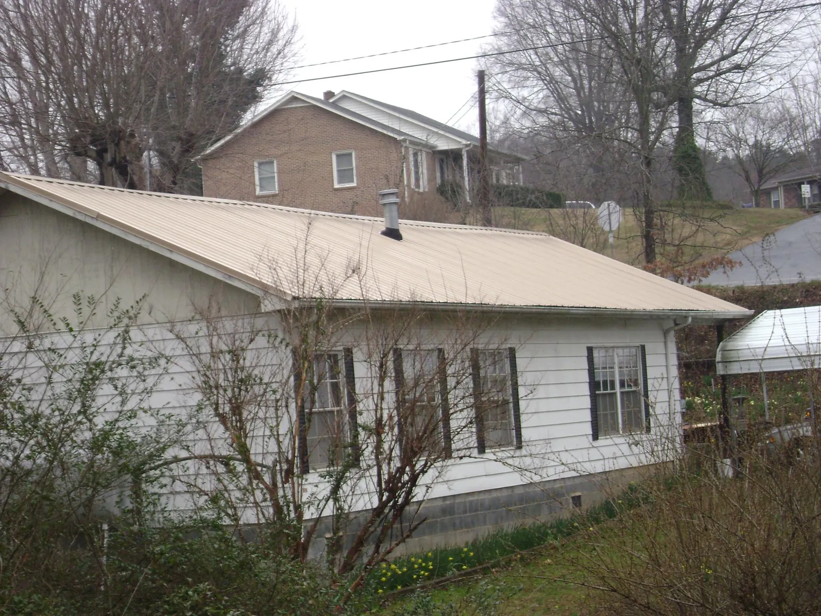 Tan metal roof on a white sided house set into a hillside — Commercial Roofing by Roofing Brothers in Port Royal